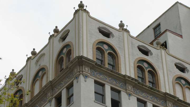 A zoomed in shot of the corner of the top floor, showing the tan-on-blue trim and arched windows with green tile