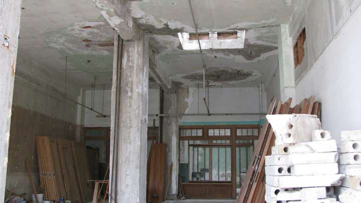 A view of another decayed room. several dozen wooden doors are stacked on the walls alongside other surplus materials.