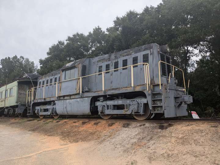 A blue-gray medium sized center cab locomotive sitting in front of a passenger car