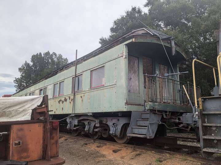 A dilapidated passenger car painted in a heavily sunfaded green, with a balcony on the end. the 3 windows on the end are boarded over, and part of a tarp hangs down from the roof