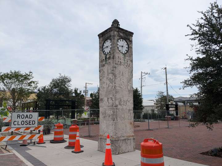 A small stone tile clocktower in an urban plaza