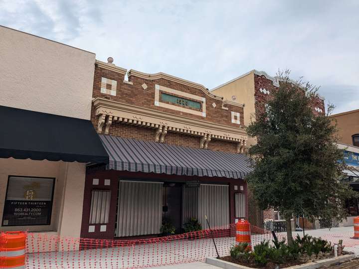 A small 1-story building, made of tan and orange tinted brick, with cream colored trim and ornamentation. 1920 is spelled out in brass letters on the top of the facade