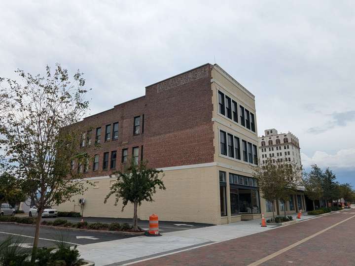 A modest 3-story brick building, with a retail storefront on the ground floor. A ghost sign on the top of the side of the building barely reads 