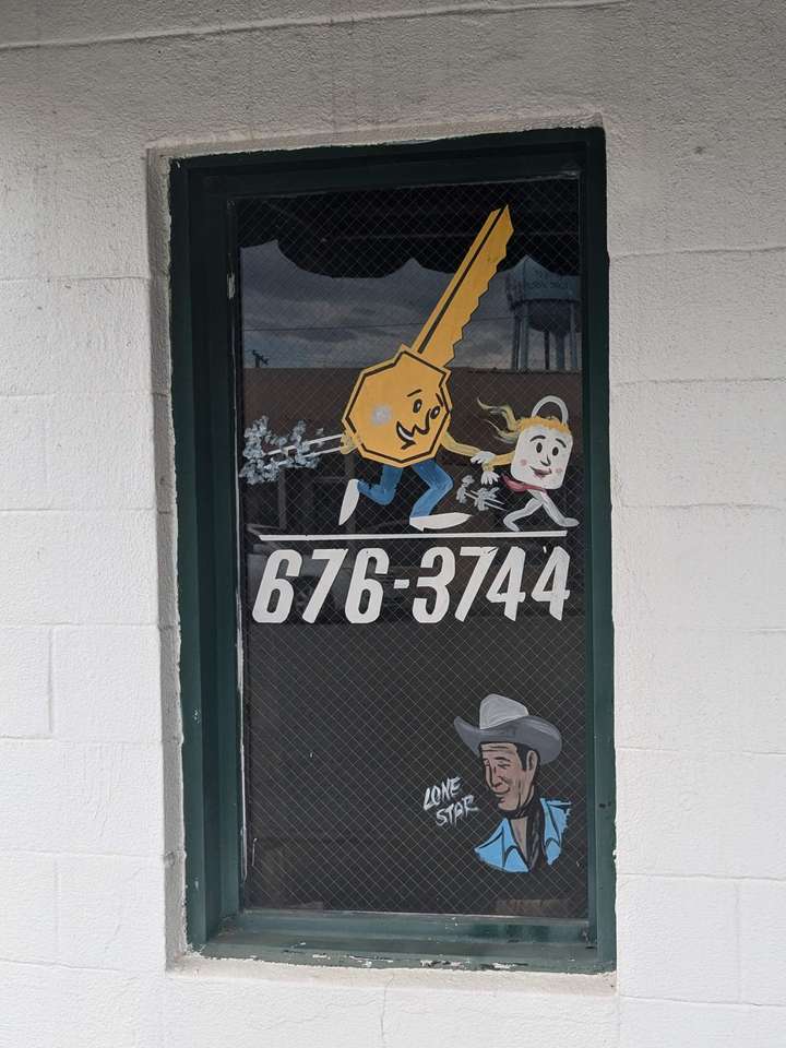 A painted window sign featuring the same key man, a lock girl, and a cowboy signature