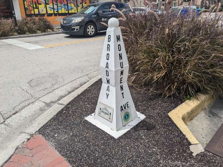 A white, pylon-style road marker. Two street names are display in vertical black text