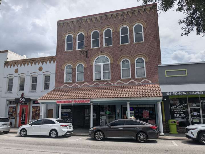 a 3-story red brick pharmacy, with an awning over the sidewalk