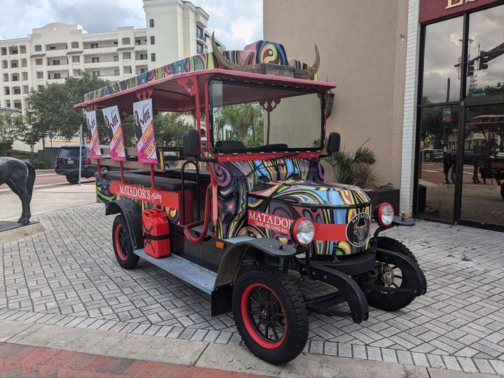 a small, 1920s-styled open bus with bench seats, painted in psychadelic colors