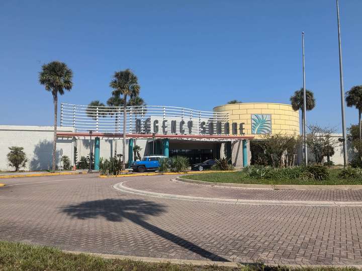 A pastel 90s mall entrance behind a large brick-paved roundabout