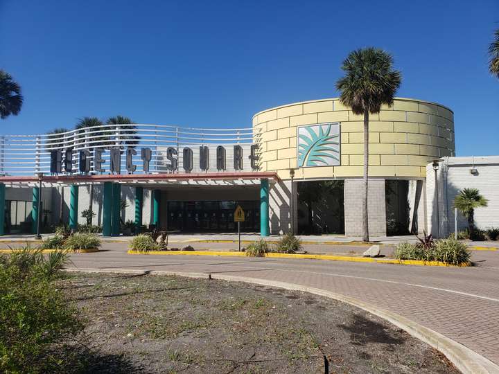 a pastel 1990s mall entrance, behind a brick roundabout.