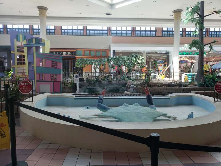 A mall center court; a large blue crab is roped off in a dry pool