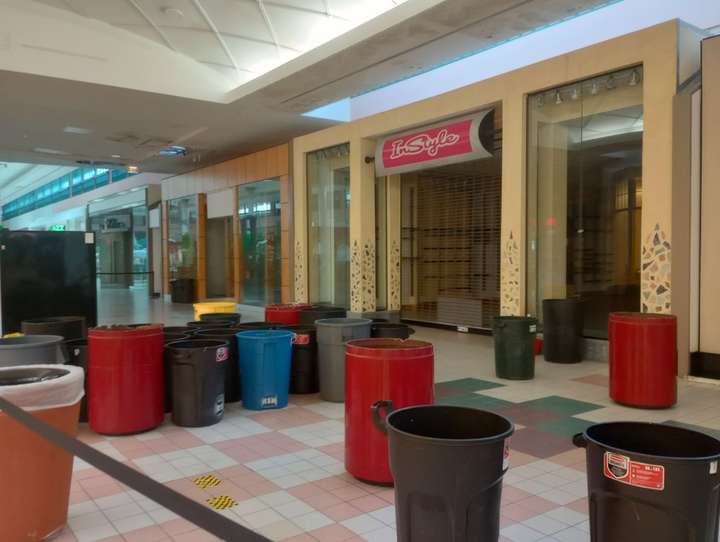 Over a dozen trash cans and barrels in front of a vacant storefront