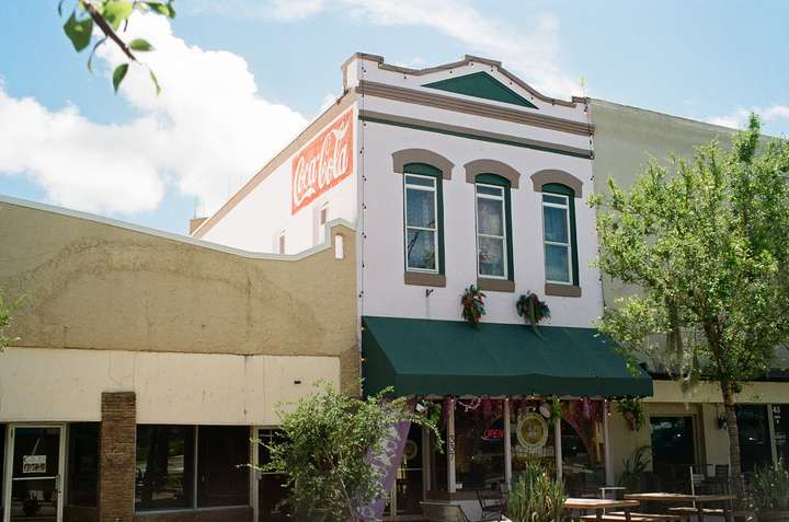 A white building with 3 windows on the top floor and an awning over a store beneath