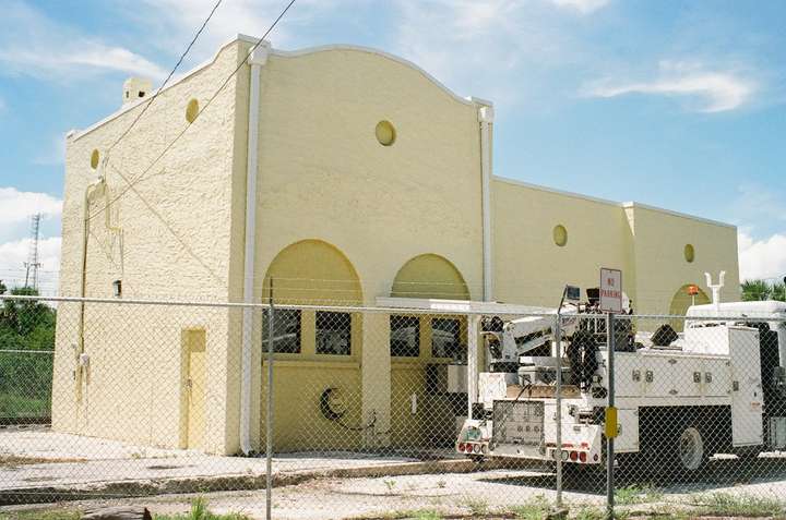 A stucco passenger station behind a chainlink fence, with a work truck in front