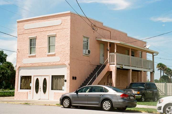 A 2-story pink building, with stairs and an elevated porch on side