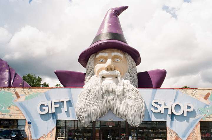 a large statue of a stereotypical wizard on top a store. 