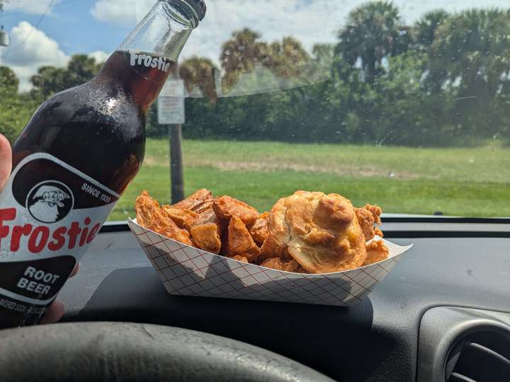 a paper basket of fried chicken and potato wedges next to a glass bottle root beer