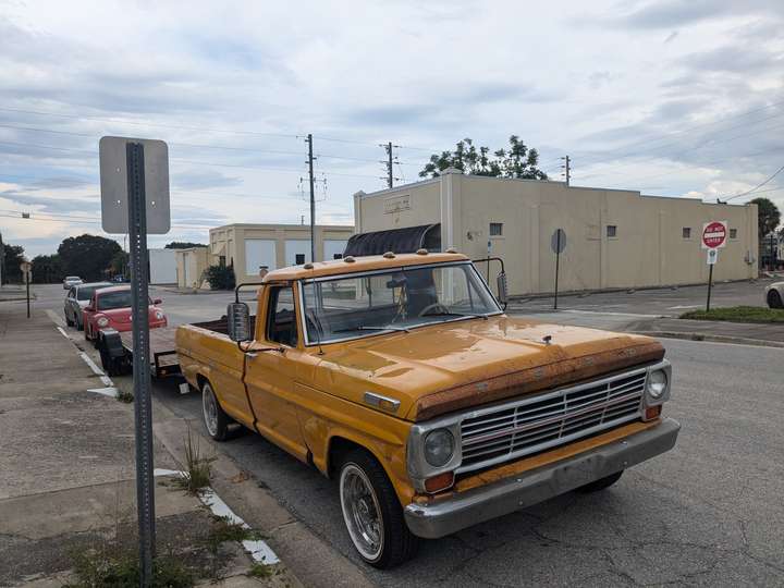 An orange vintage pickup truck next to a street sign