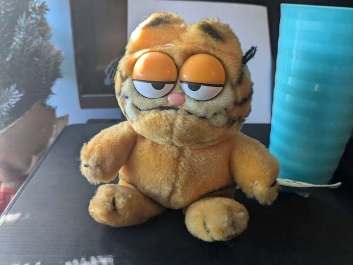 A slightly scrubby Garfield plush sitting on a printer