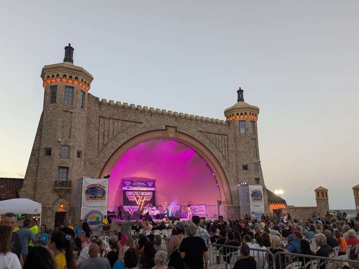 A Spanish Revival styled bandshell lit with pink lights and a crowd in front