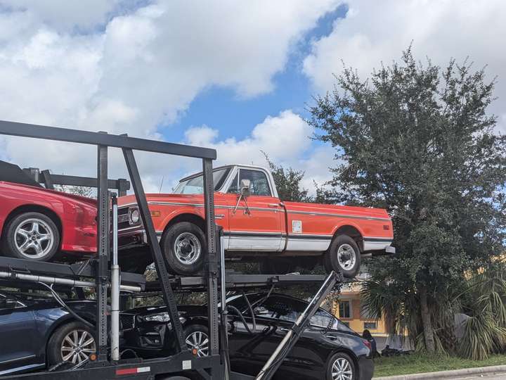 An orange pickup truck with a white lower stripe and cab on a car carrier