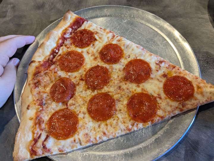 A large slice of thin pepperoni pizza, sitting on a thin metal plate