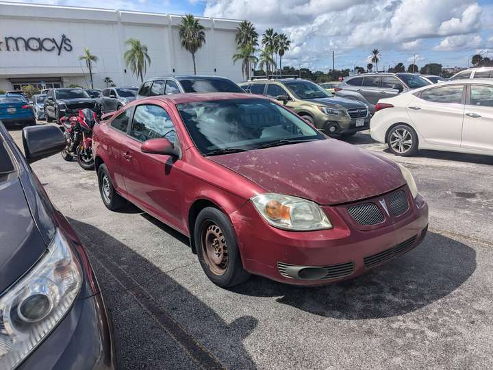 A red coupe with a weathered hood and no hubcaps