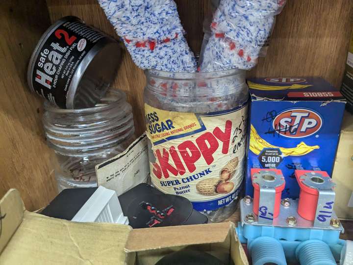 An empty peanut butter jar being used to hold cleaning brushes