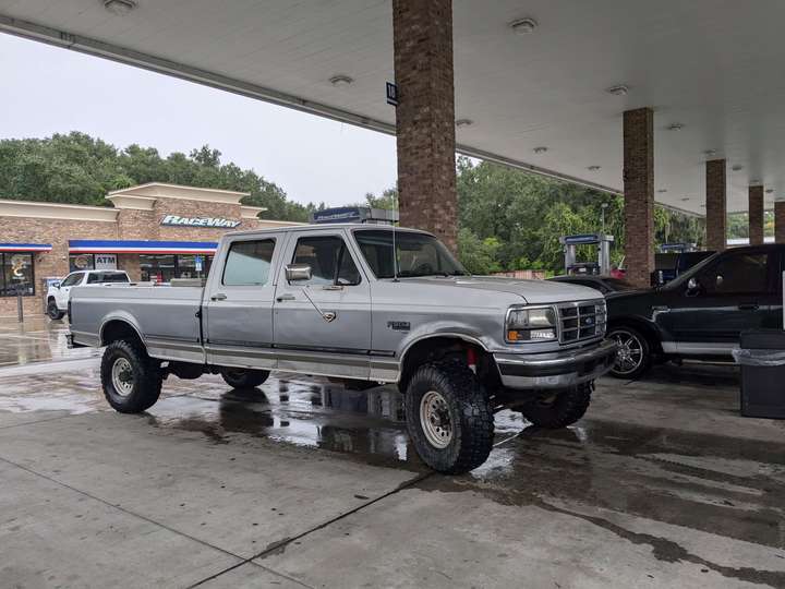 A long, slightly lifted dual-cab pickup truck at a gas station