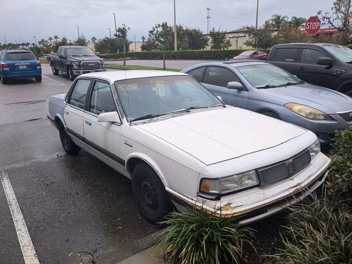 A white sedan with a primer gray rear quarter panel and a weathered bumper