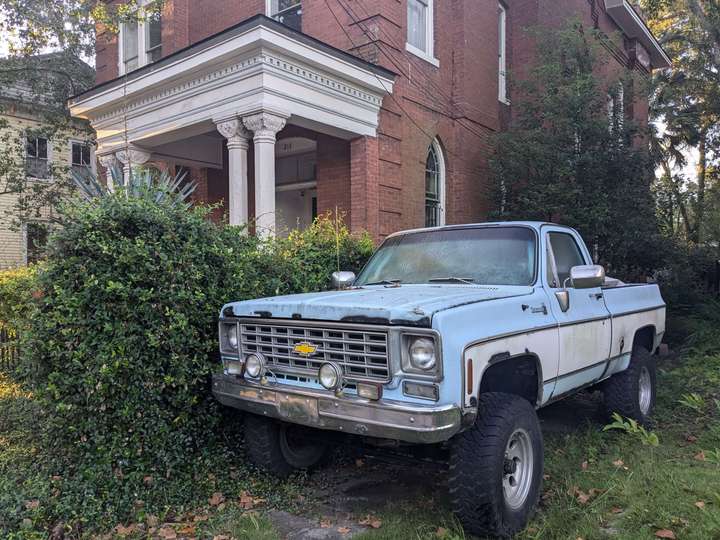 A sky blue lifted pickup truck with white accents parked alongside a brick house