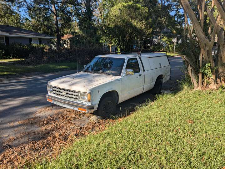 a street-parked weathered white minitruck with a bed cover