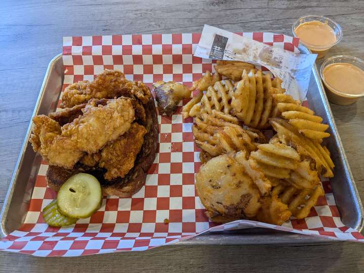 fried chicken served on a slice of bread with waffle fries, on a metal tray