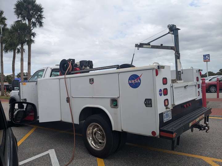 A long white pickup truck with a service bed, crane, and air compressor