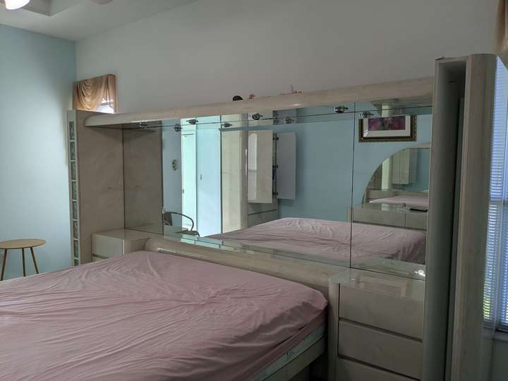 A bed w/ pink sheets with a mirror headboard framed by pearl-color drawers