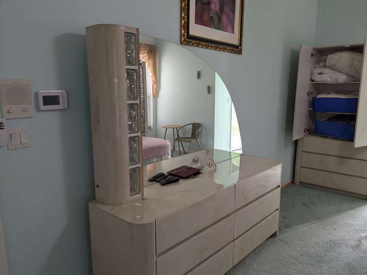 A rounded dresser with a quarter-circle mirror in a marble-pearl color