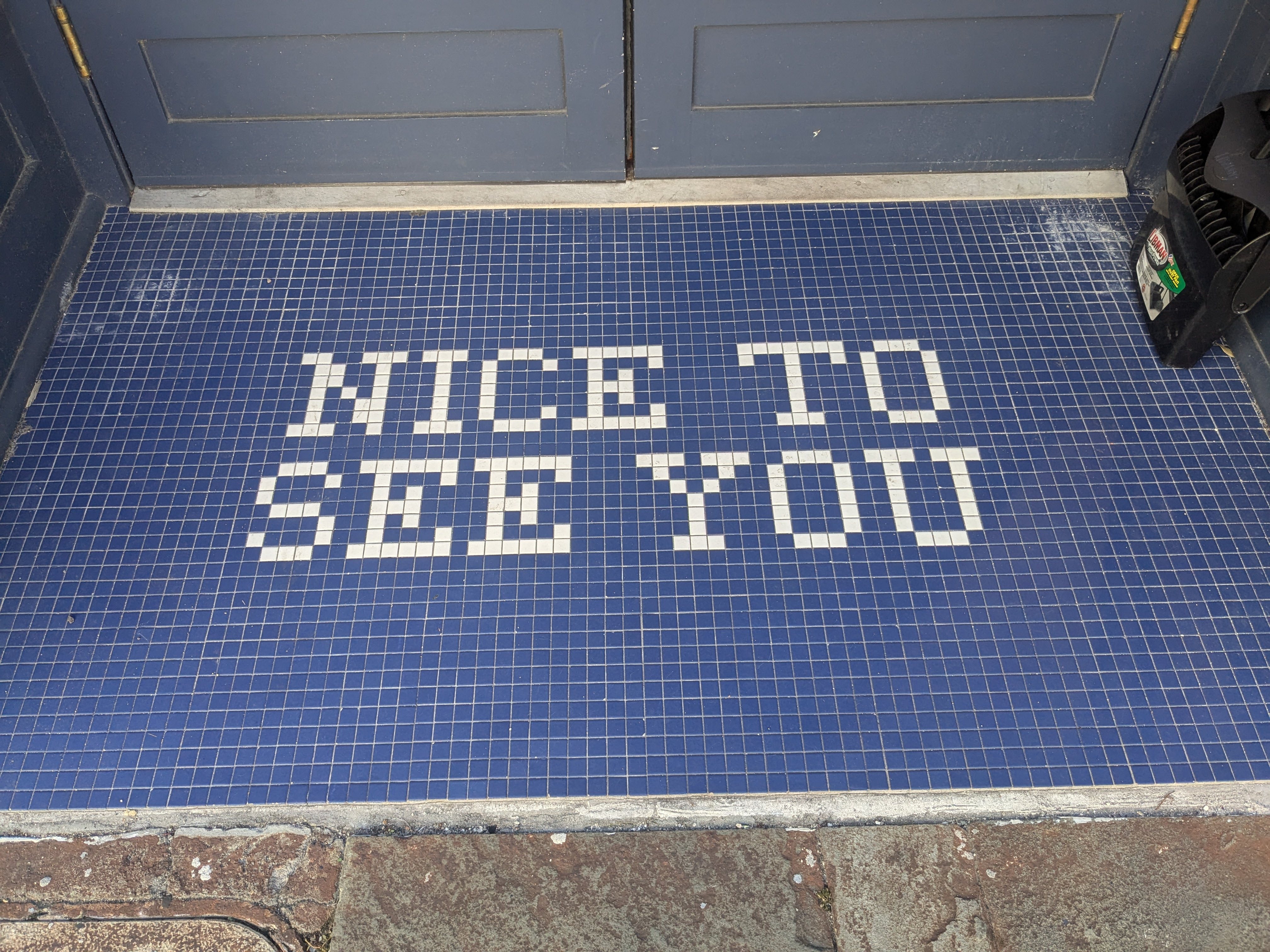 NICE TO SEE YOU is spelled in square, white tiles against a background of solid blue tiles