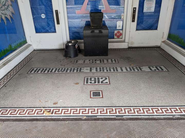 Red lettering spells out F.T. Smith Hardware-Furniture Co, trimmed with a thin line. the whole entrance is outlined in a wave esque pattern