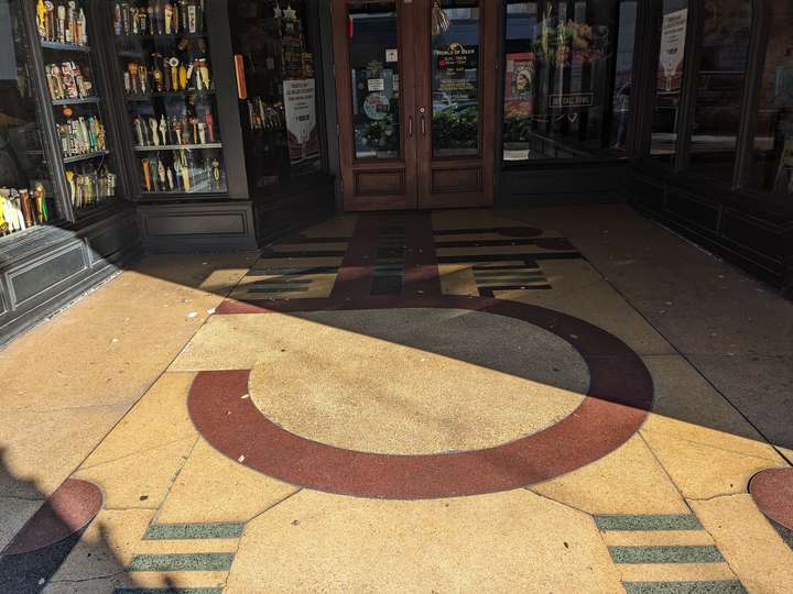 A large, red, hook like shape in the center, surrounded by patterns of lines, inset on a sand yellow floor