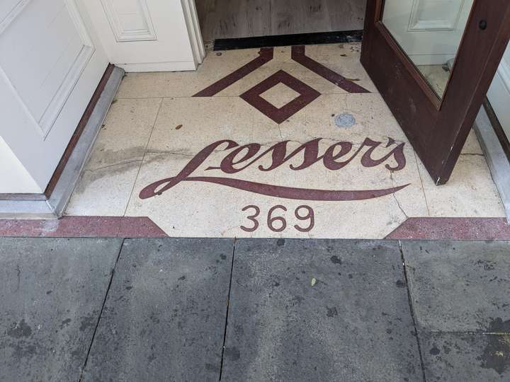 A hexagonal pattern of a diamond framed by two lines, above 'Lessers' in red script font. The bottom tail of the L extends the length of the word