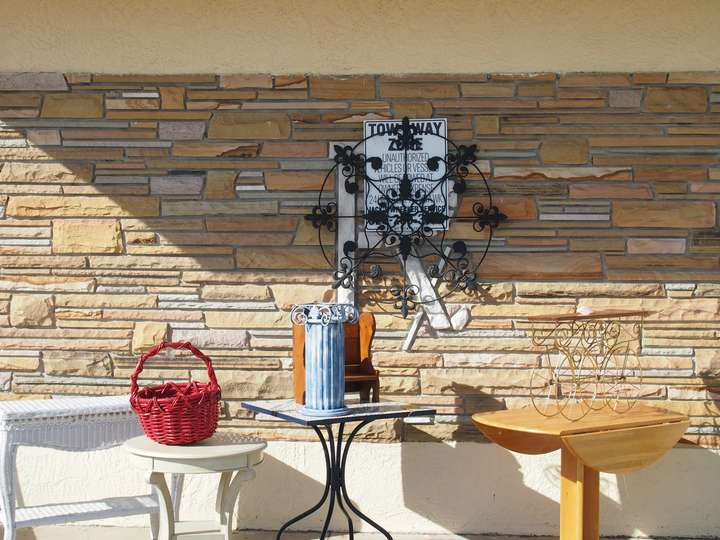 Rx spelled out in white tile on a background of irregular sandstone bricks. Hanging antiques and a poster obscure it, as does furniture in the foreground