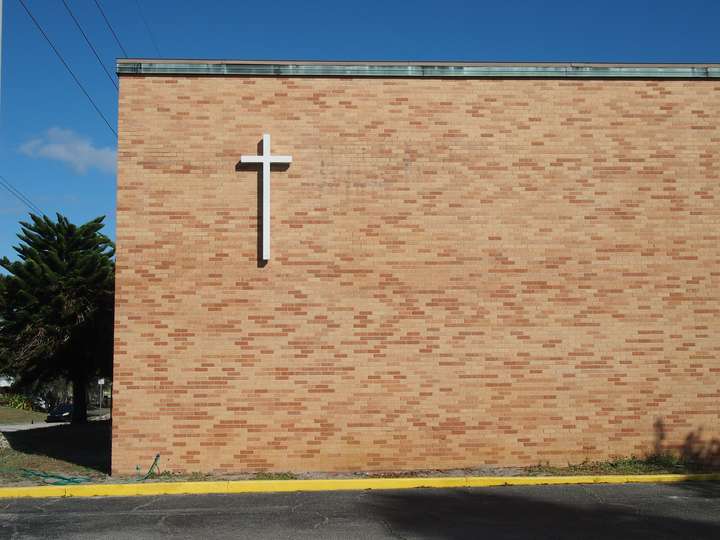 A head-on shot of a brick wall with a simple white cross in the upper left