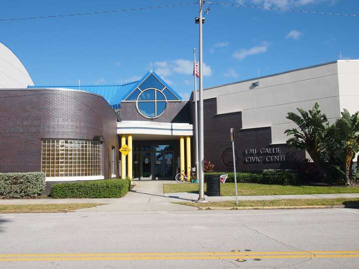 A post-modern building entrance. Smooth yellow columns support a curved canopy in front of a entrance with a triangle peaked roof.