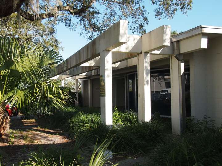 A small brutalist canopy covering an overgrown courtyard