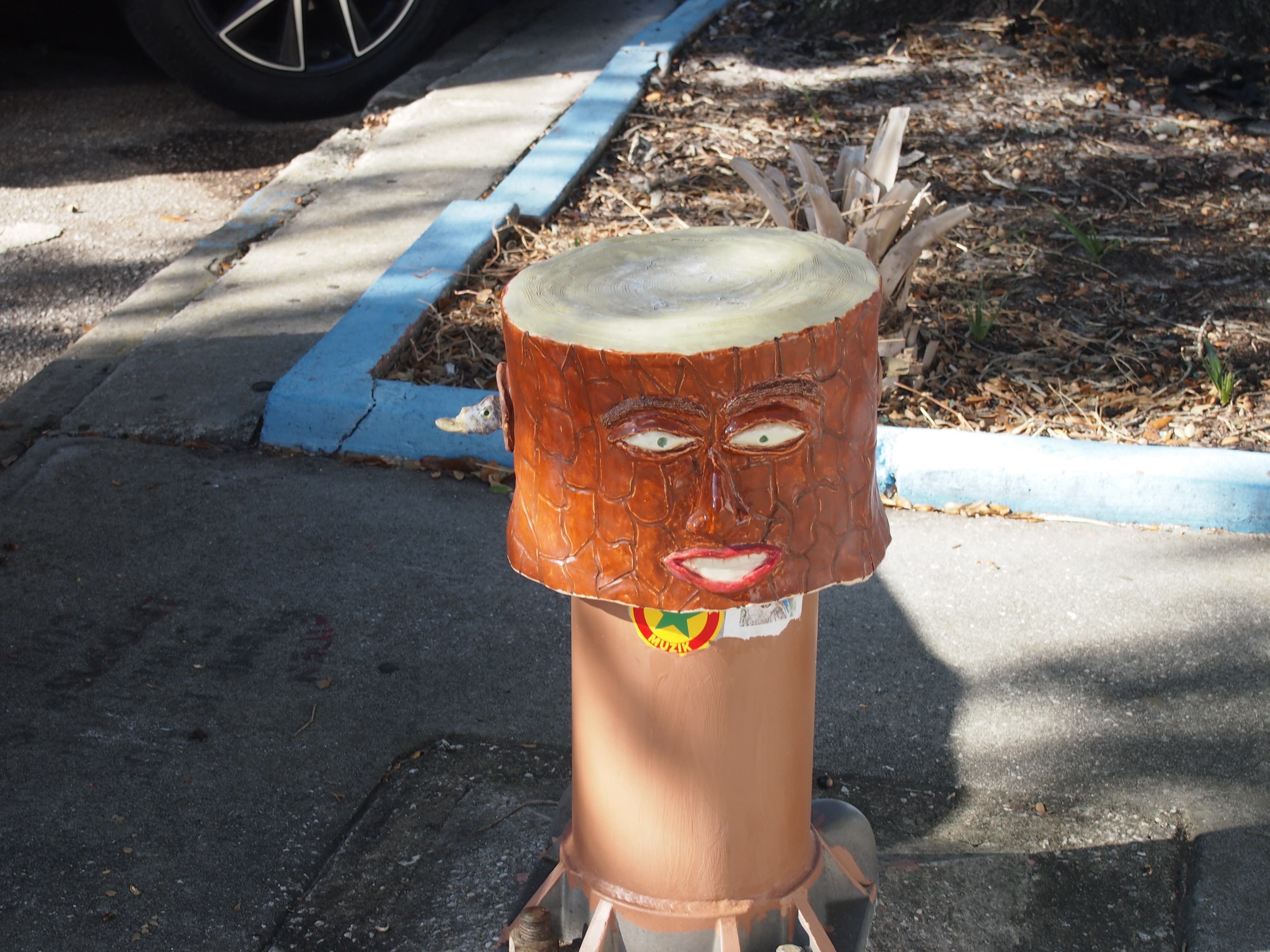 A weird looking statue of a tree stump with a face, on top of some kind of bollard or post