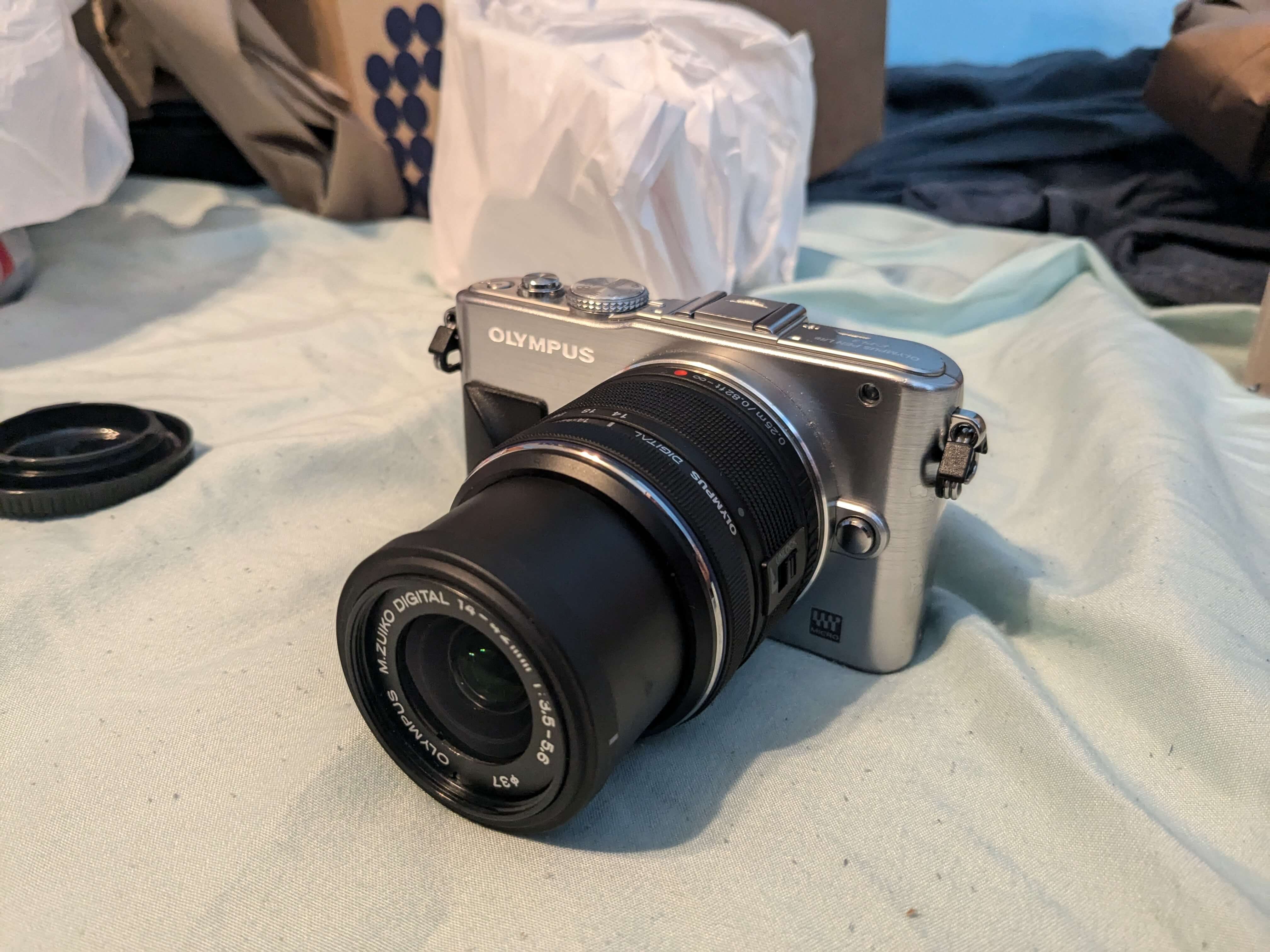 A silver digital camera with a black lens, sitting on light blue sheets