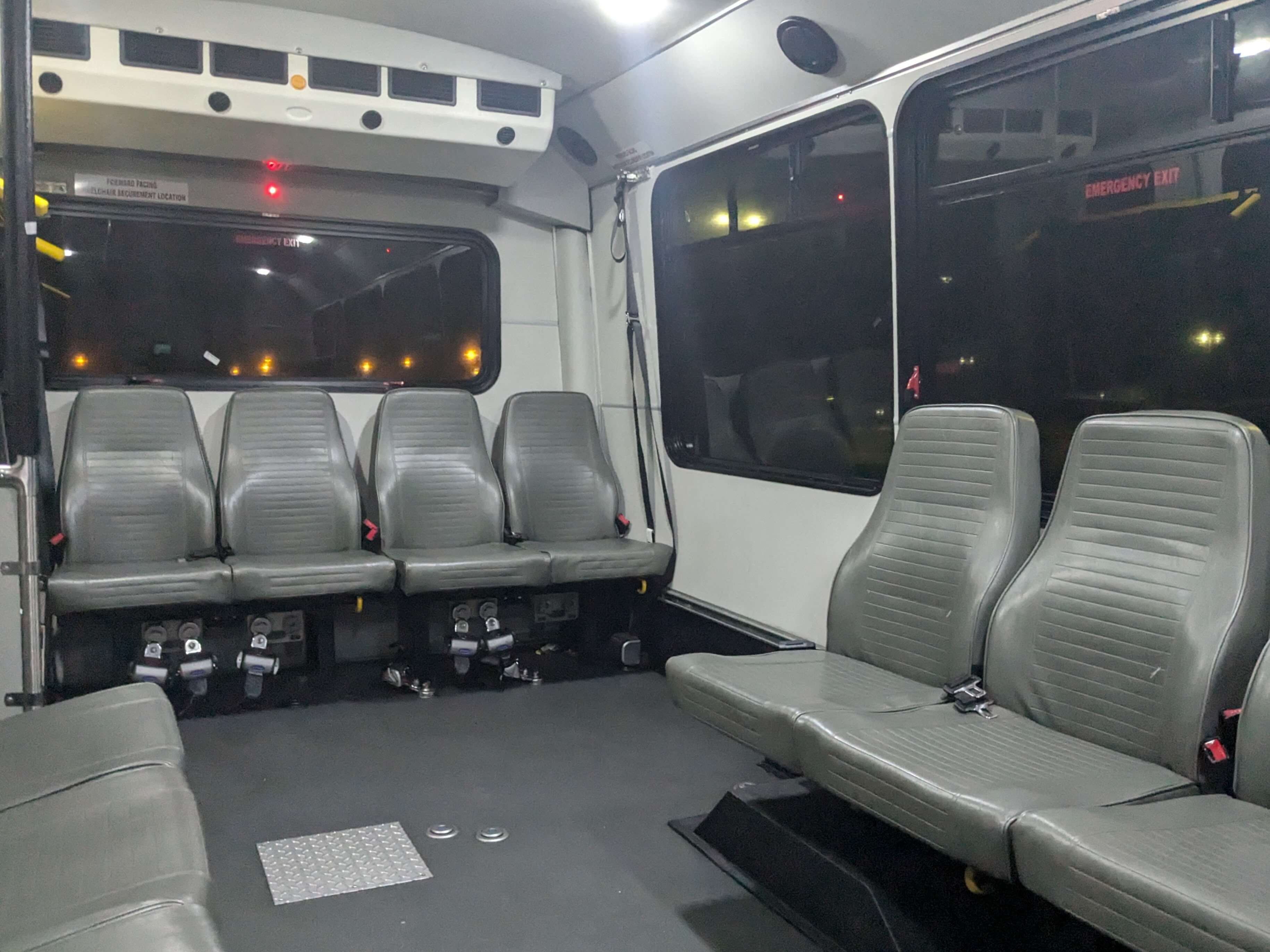 the empty interior of a minibus. The floor is dark gray, the walls white, and the seats are light gray faux leather