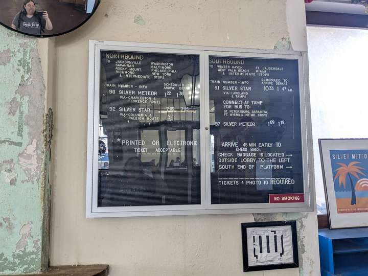 A departure board made up of white plastic letters arranged on a ridged back board