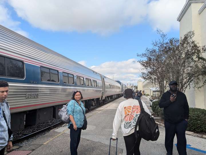 Passengers mill about on the platform after disembarking from the stainless steel passenger train in the background