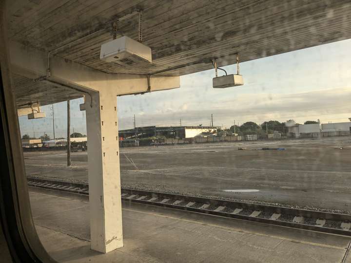 A view out a window stained with waterspots, showing a station canopy and a large gravel lot