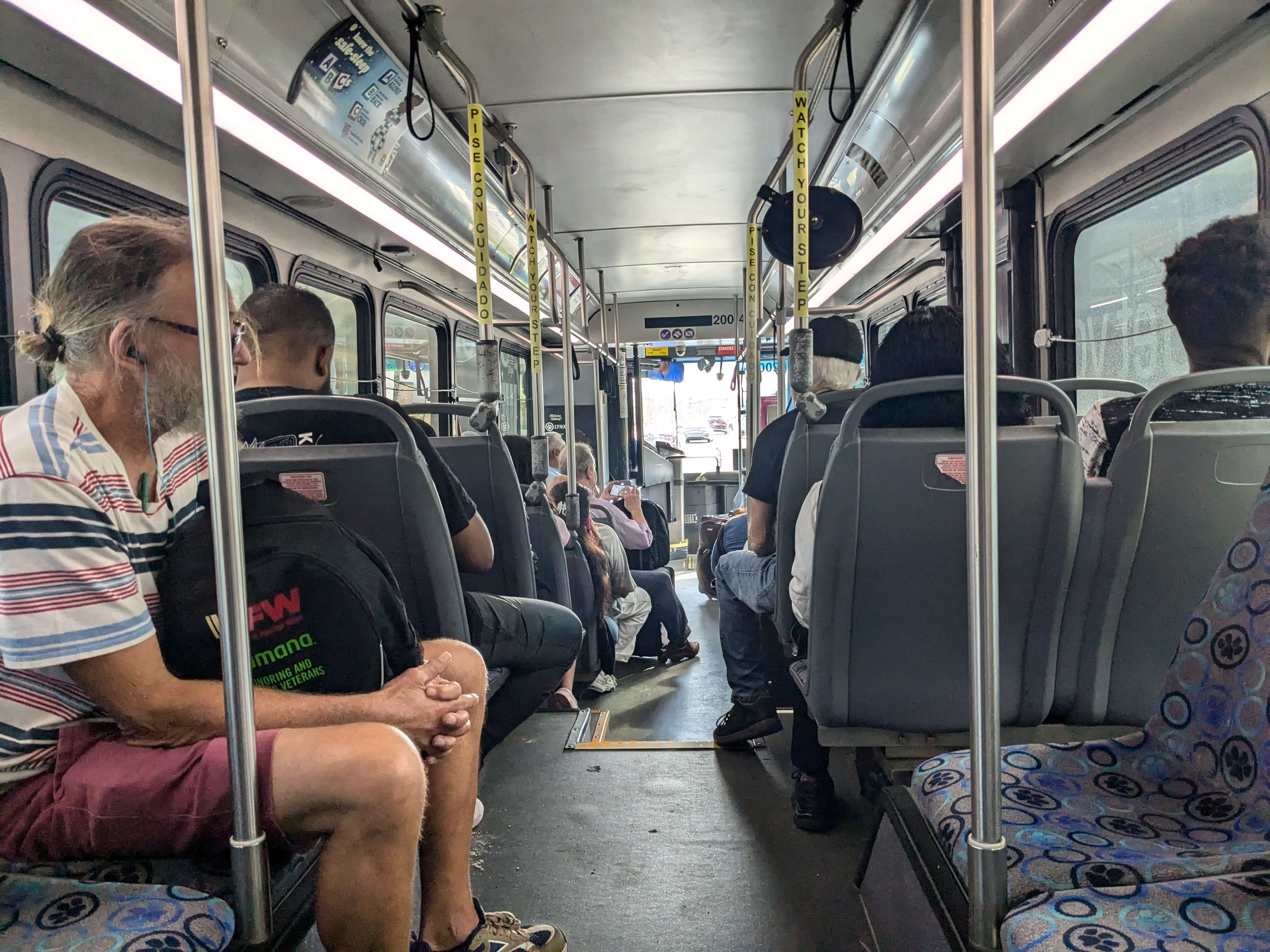 The crowded interior of a city bus. The seat print features multi-color paw prints.